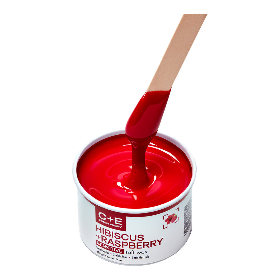 Red wax being poured into a container labeled 'C+E Hibiscus + Raspberry' on a white background.